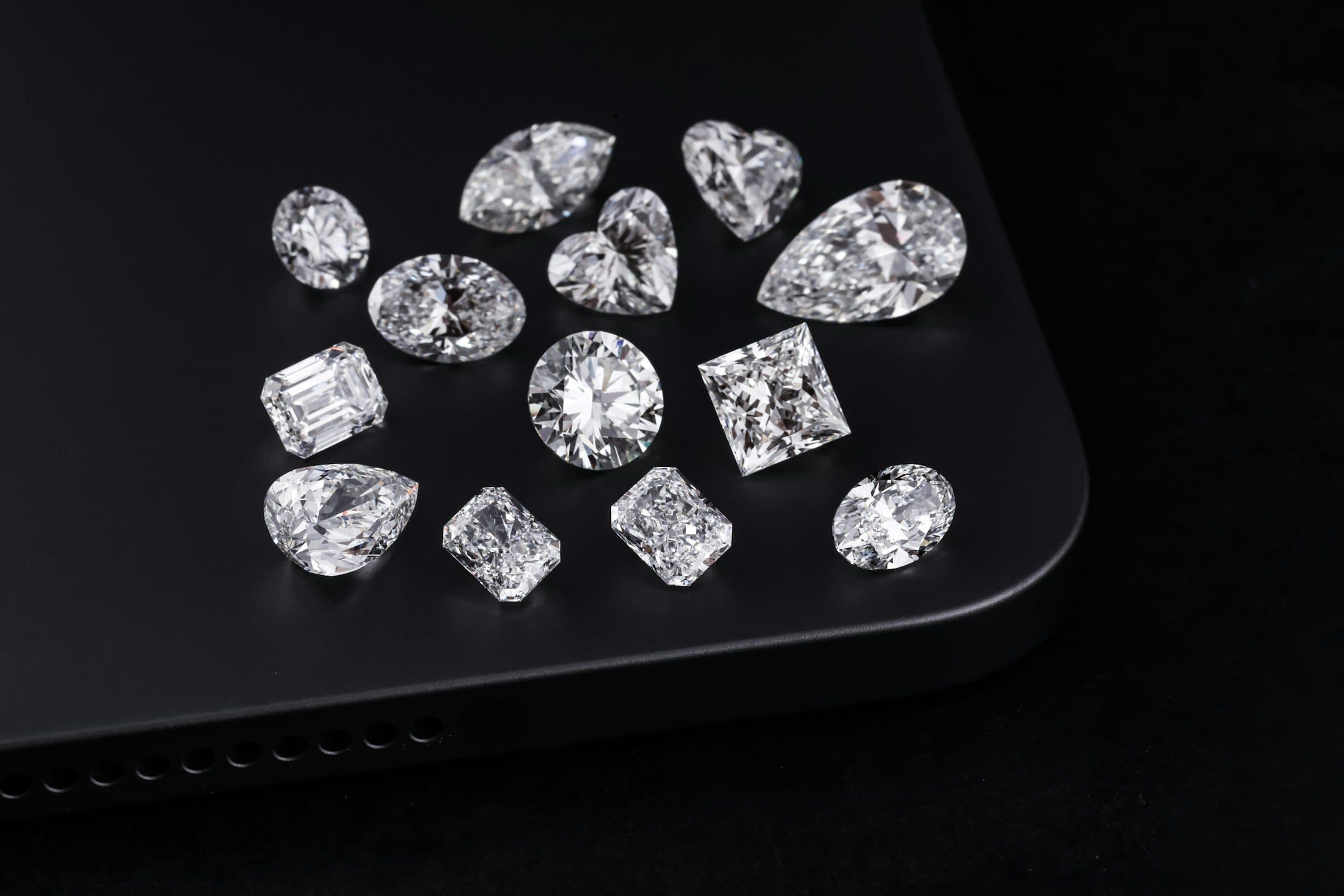 Thirteen diamonds of different cuts arranged on a black surface