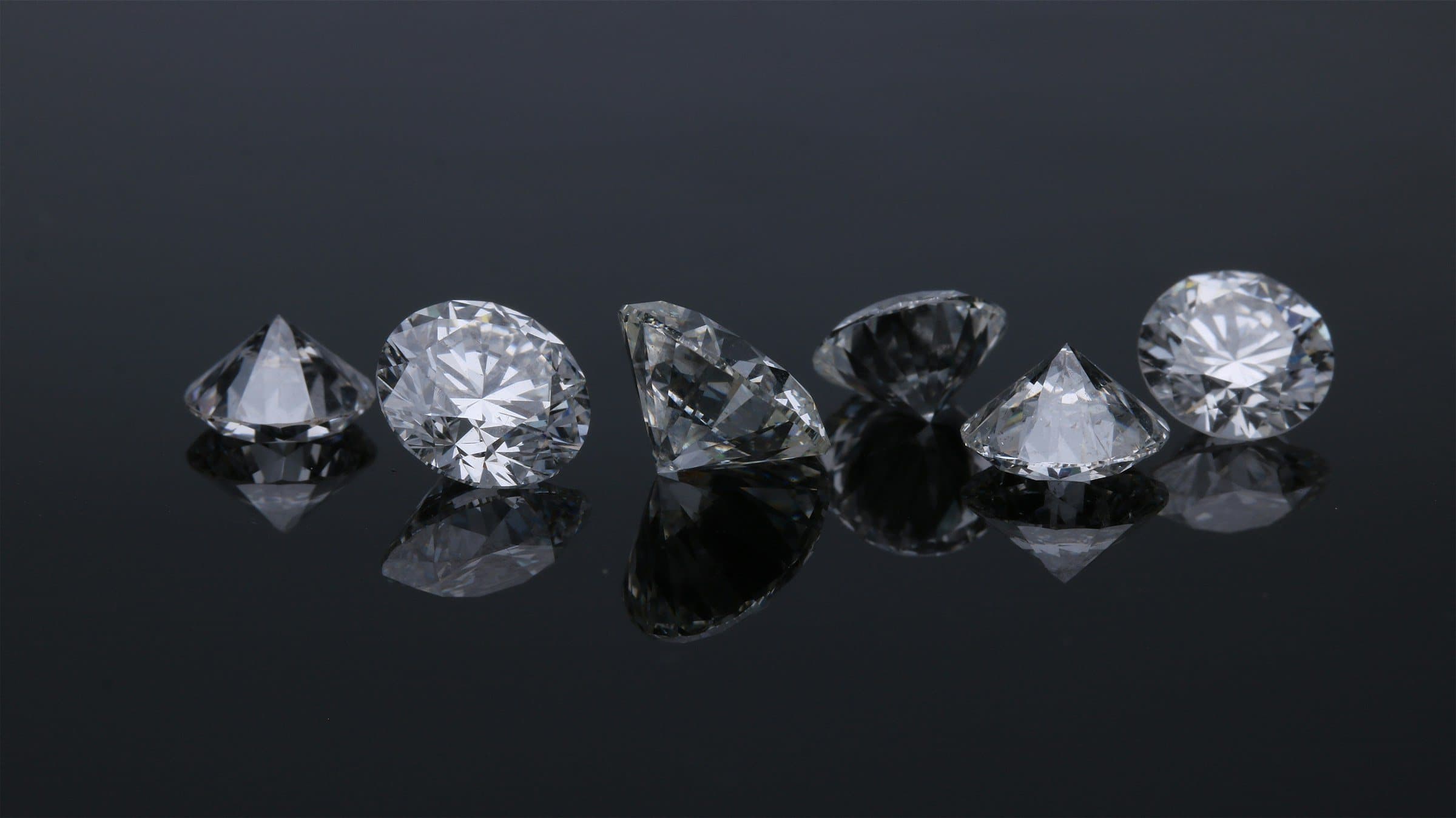 Six cut diamonds in a row on a dark reflective surface