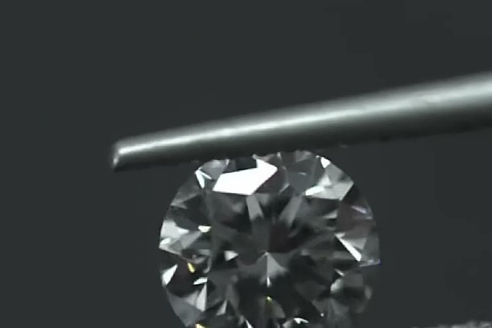 A finished brilliant-cut diamond held in tweezers
