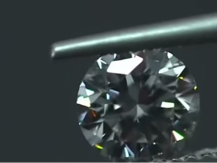 A finished diamond examined under a probe against black