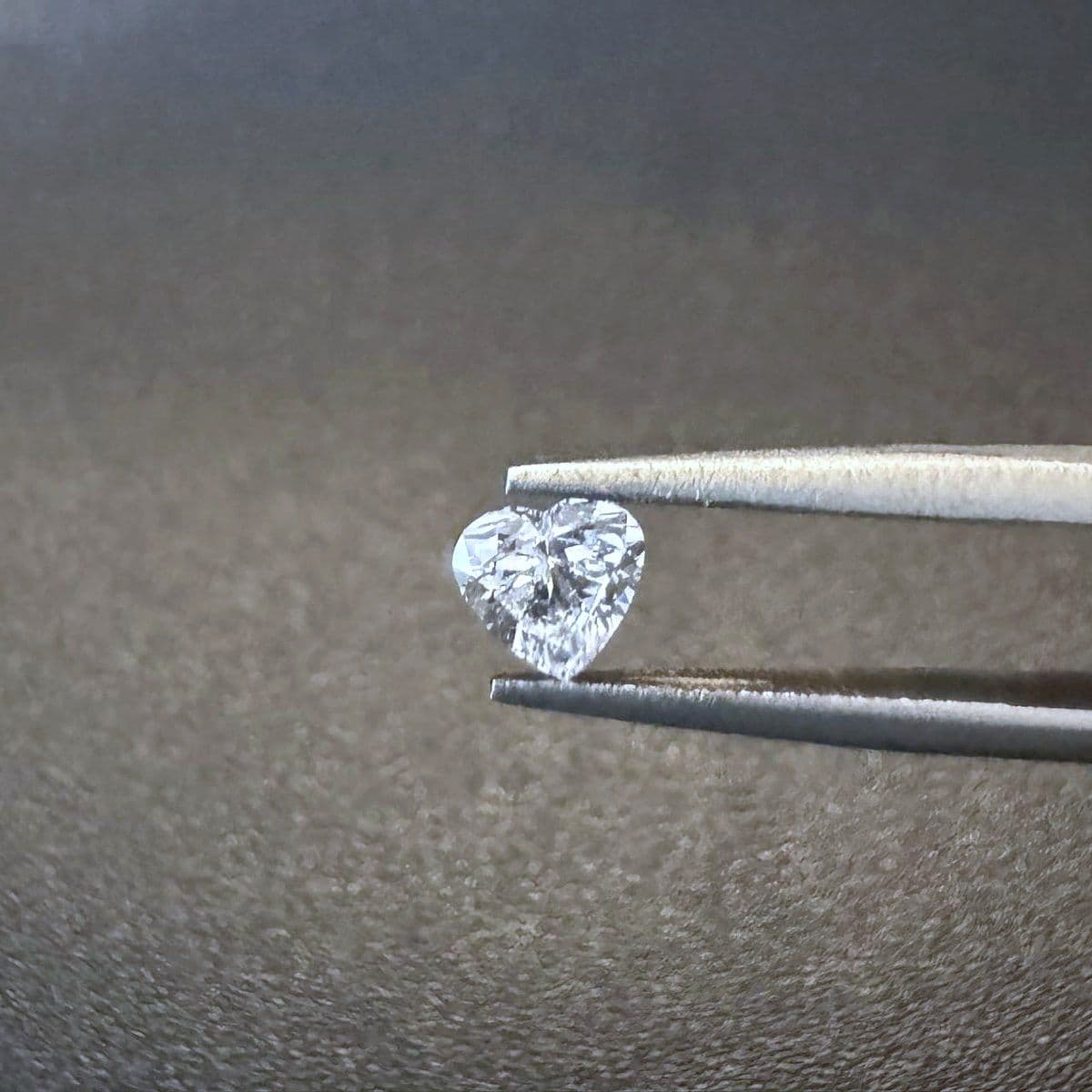 A heart-cut Everlong Gem diamond held in tweezers