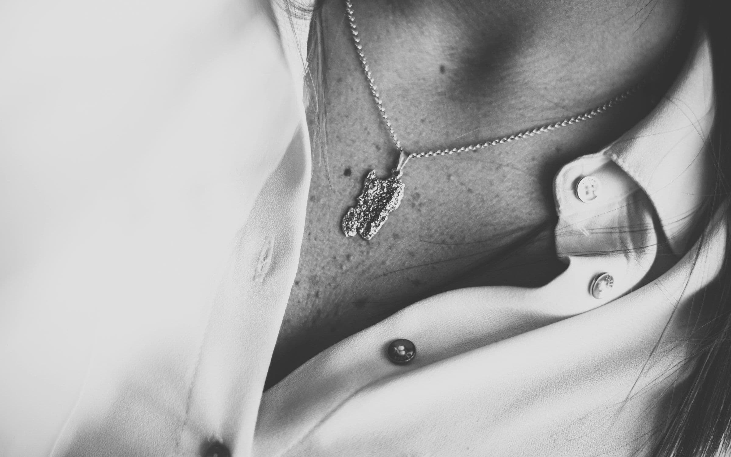 A raw stone pendant on a fine chain, worn against a white blouse — in black and white
