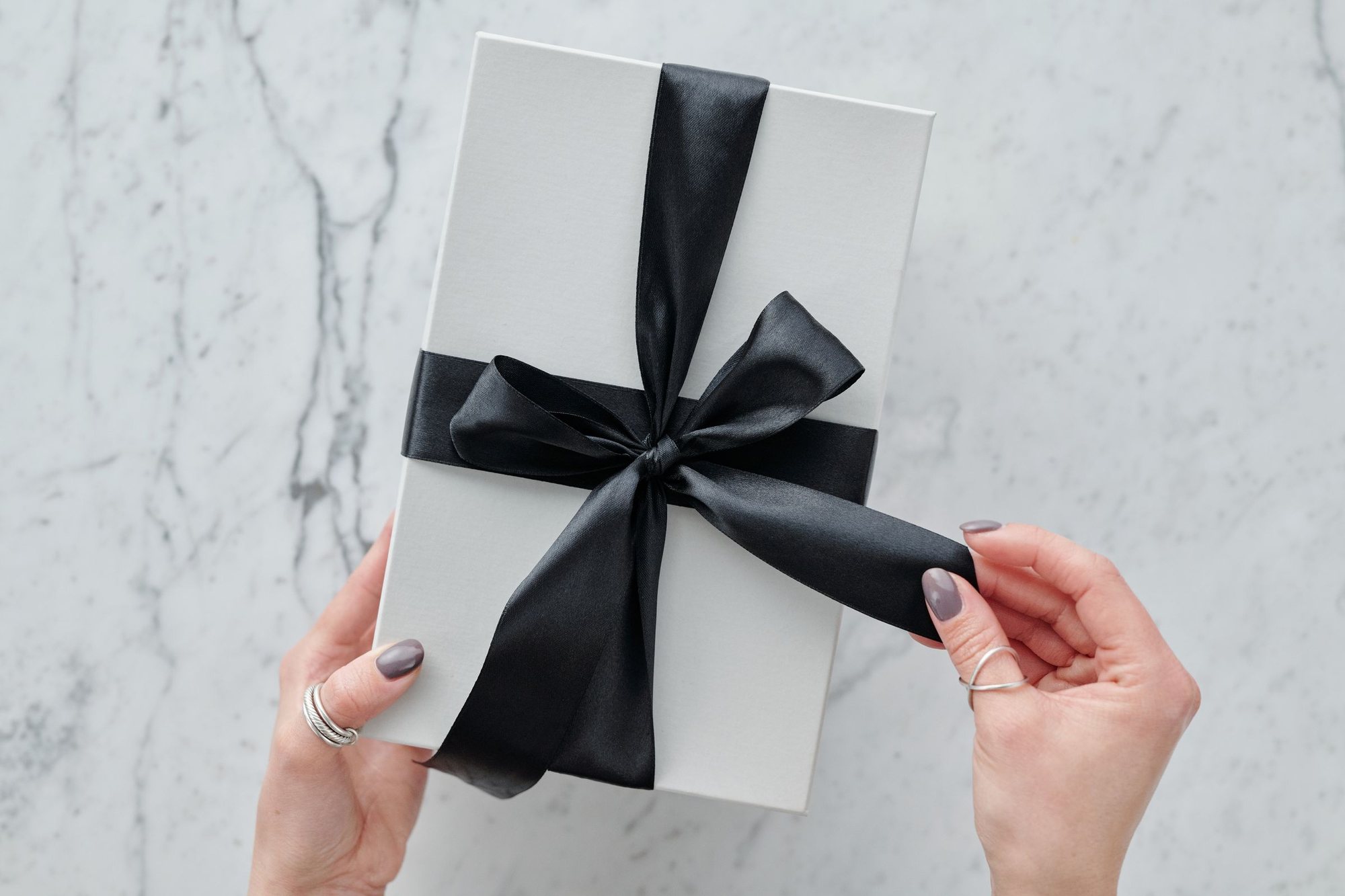Hands gently untying the black ribbon on a white gift box
