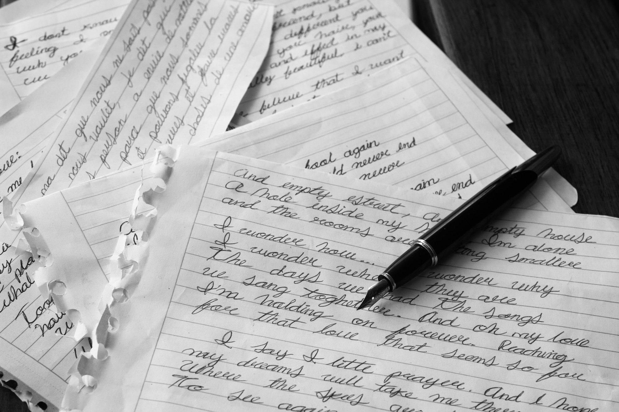 Handwritten letters spread beneath a dark fountain pen, in black and white