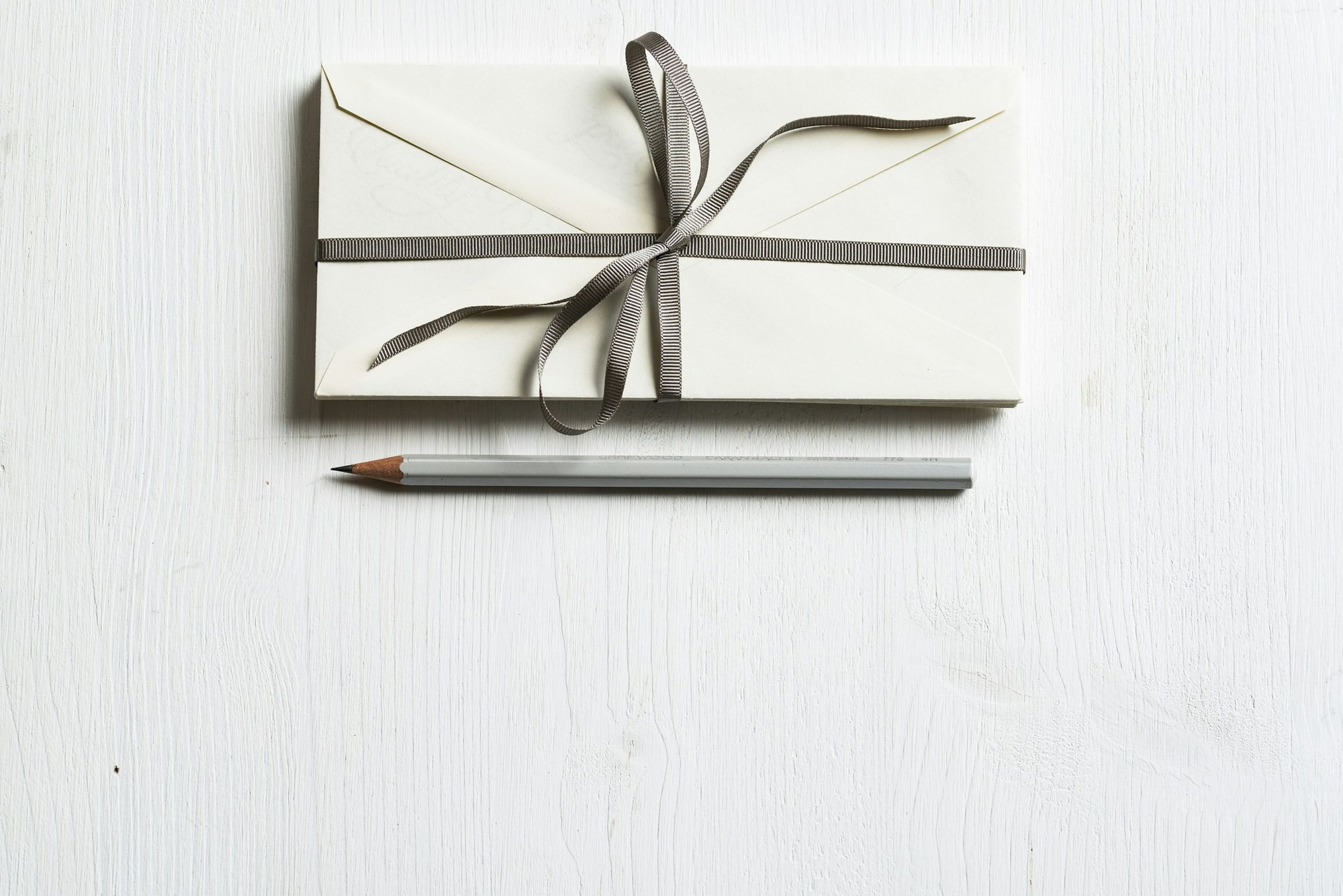 Ivory envelopes tied with a grey ribbon, a grey pencil beside them