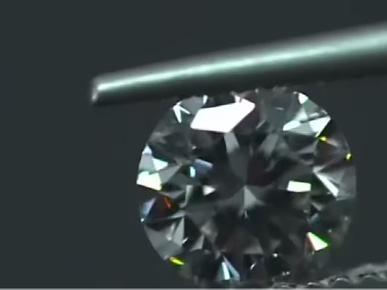 A finished diamond examined under a probe against black