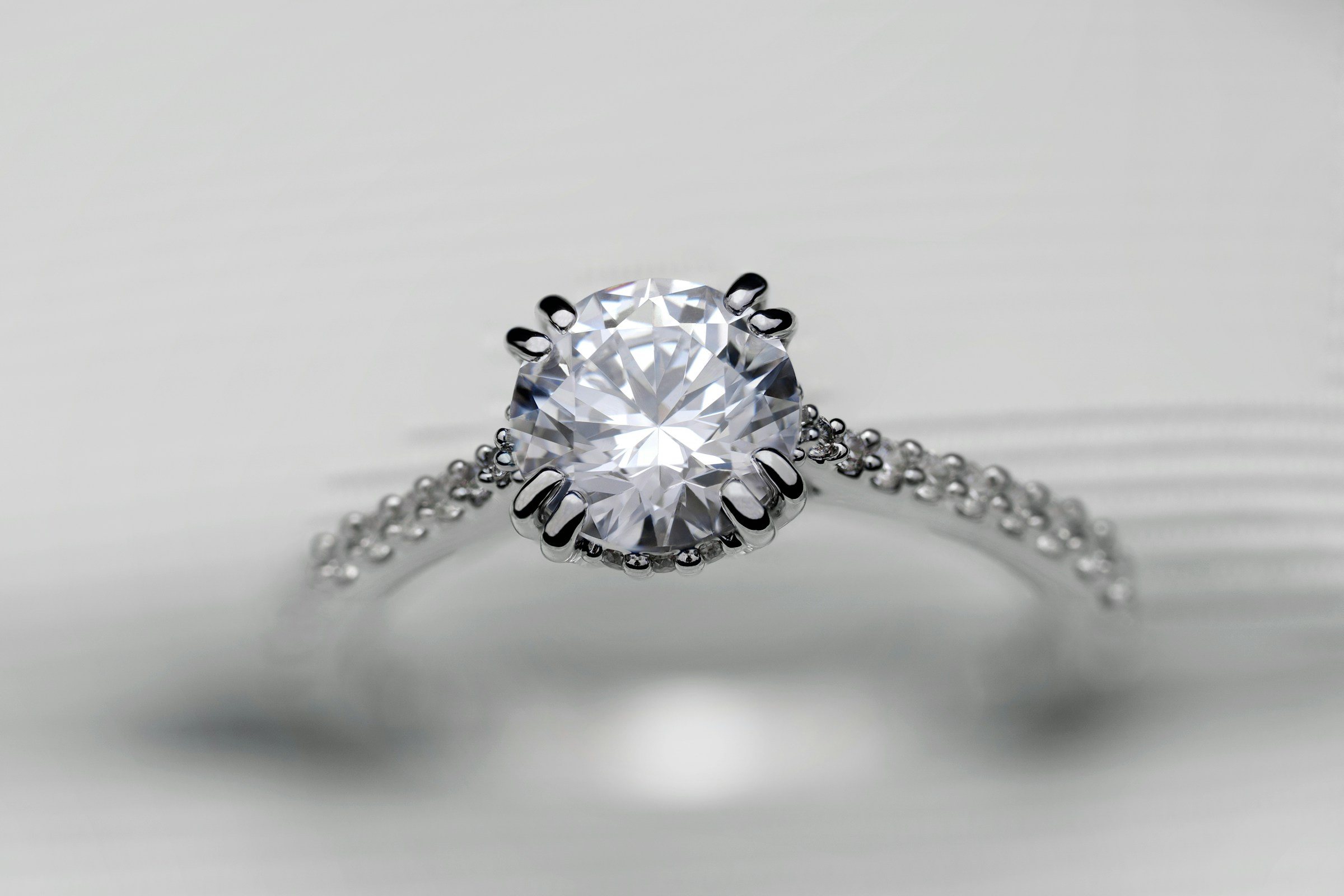 A platinum solitaire diamond ring resting on a soft white surface