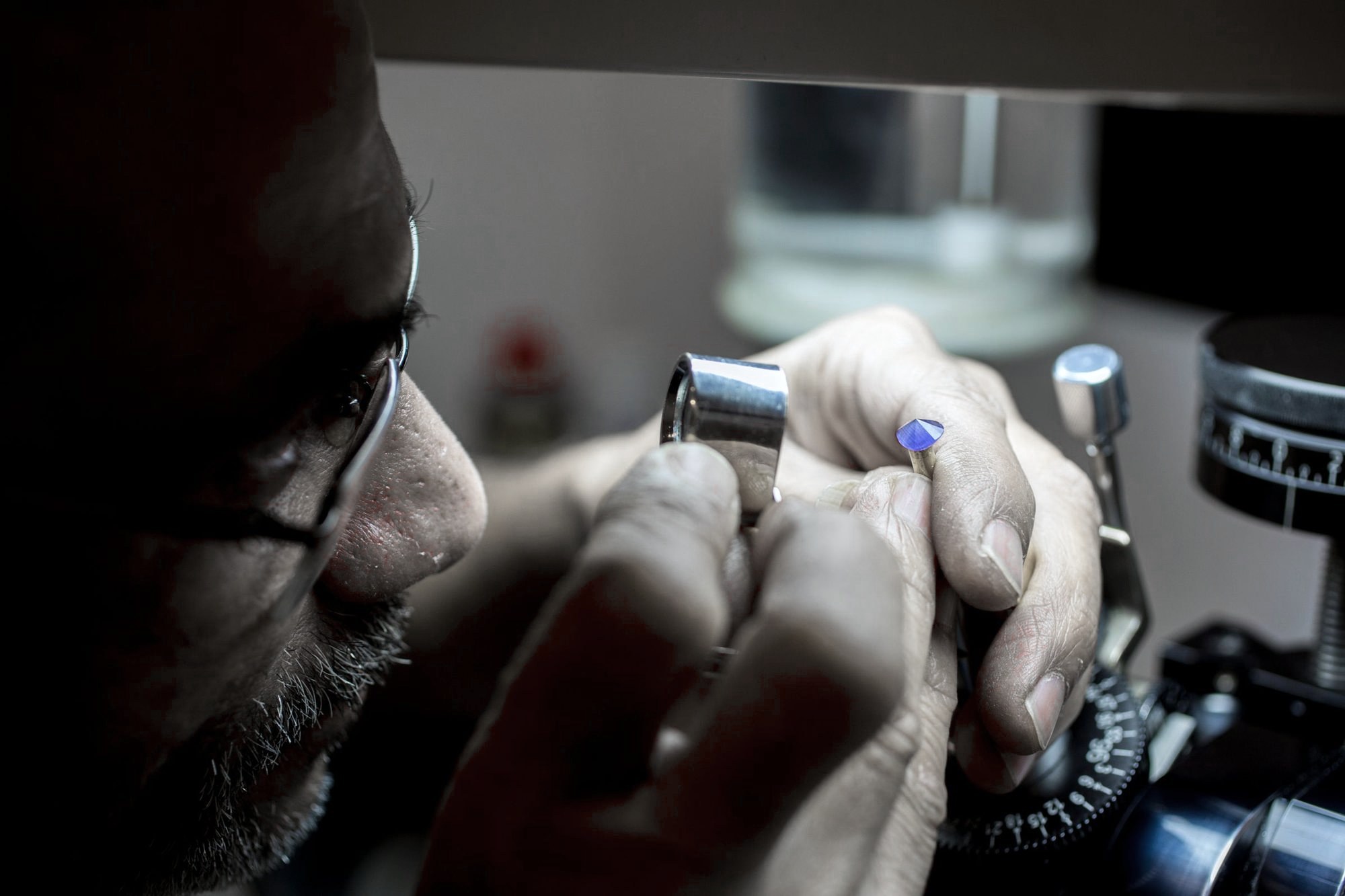 A gem cutter examining a stone through a loupe at the faceting bench