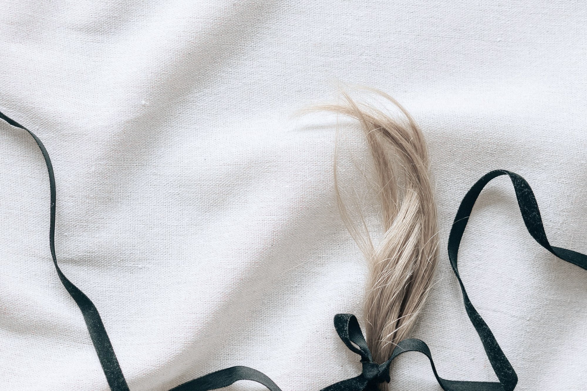 A braid of hair tied off with a black ribbon, resting on ivory linen
