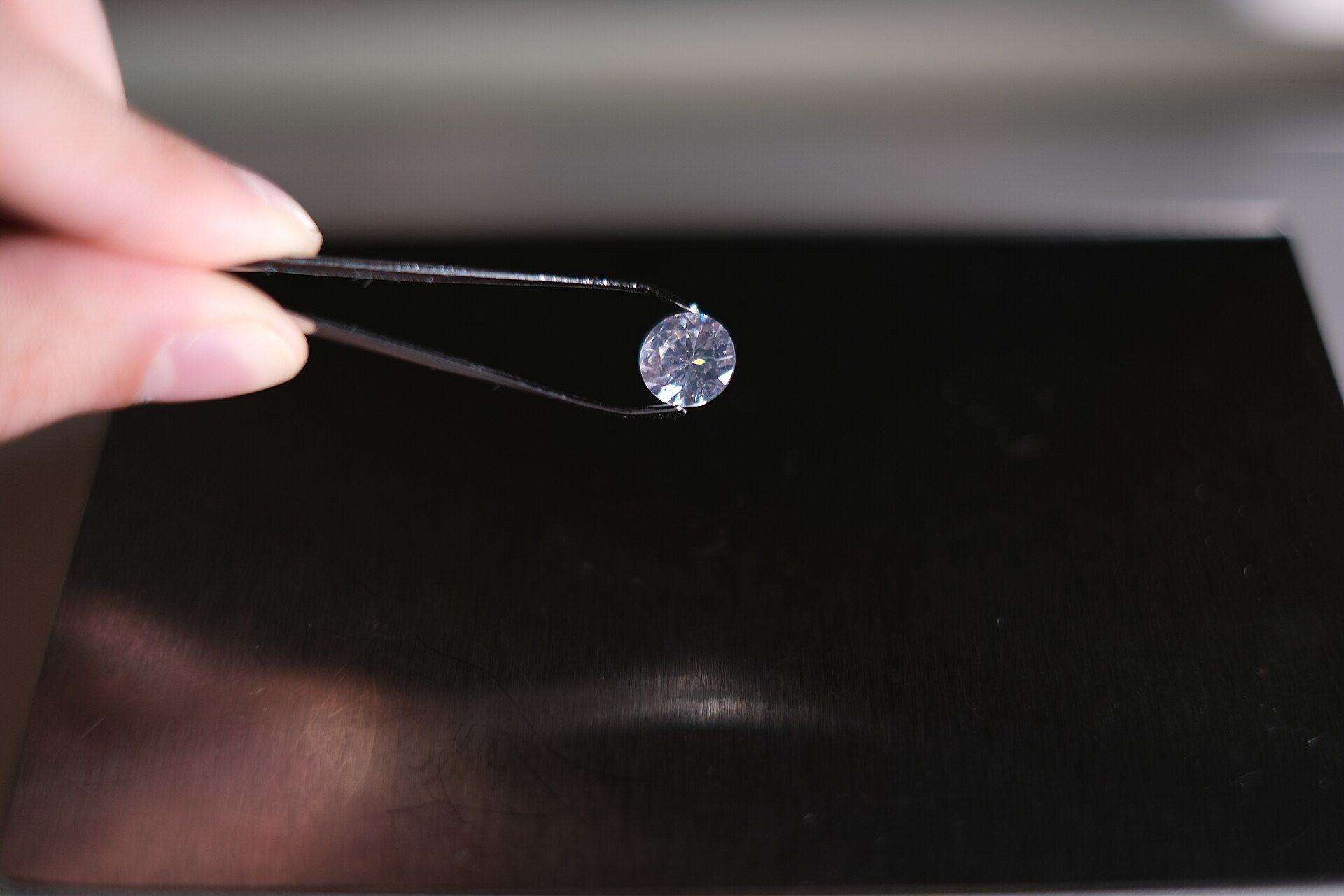 A diamond held in tweezers over a dark grading table